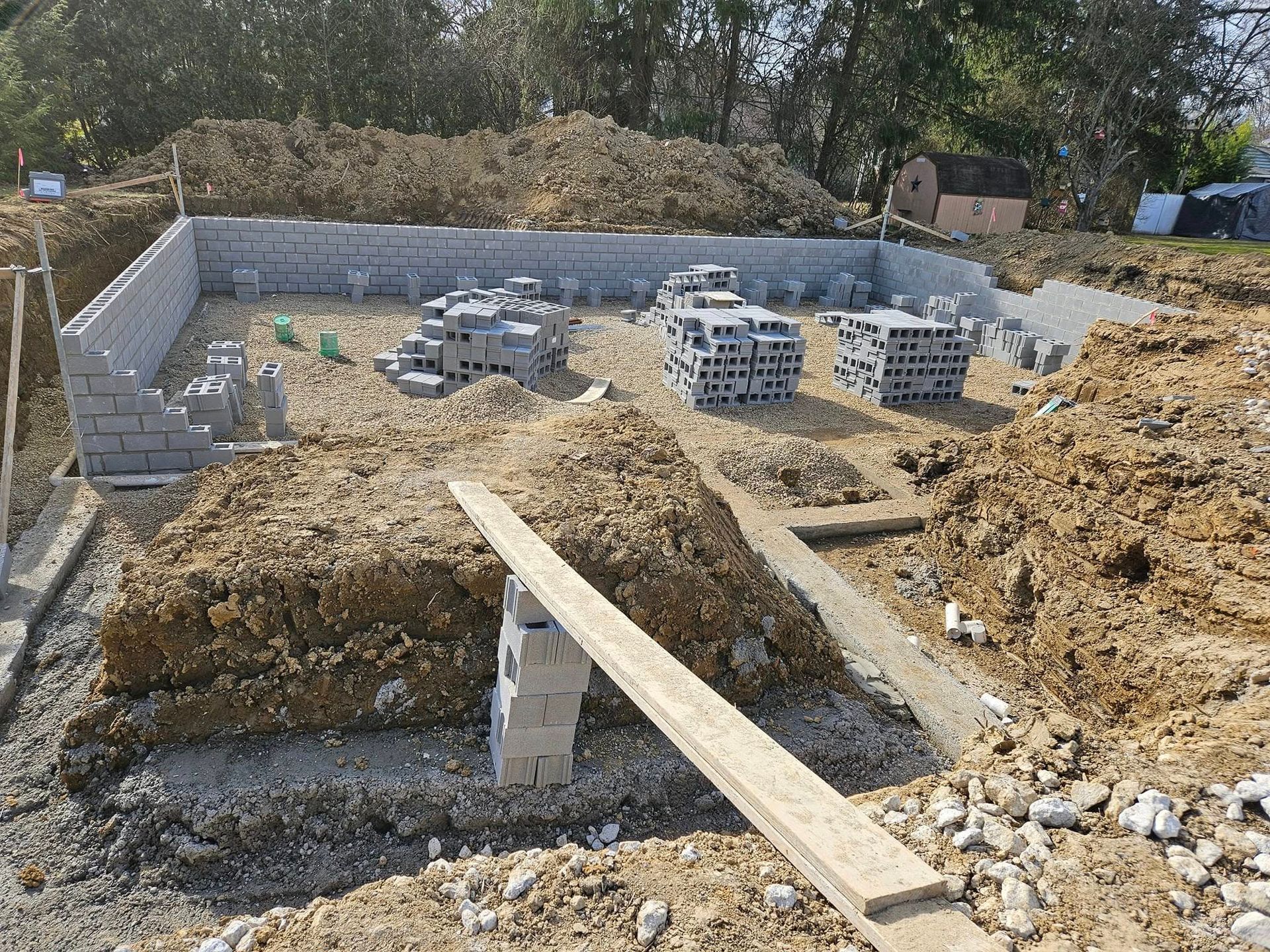 Construction site: cinder block foundation partially built, dirt piles, stacked blocks.