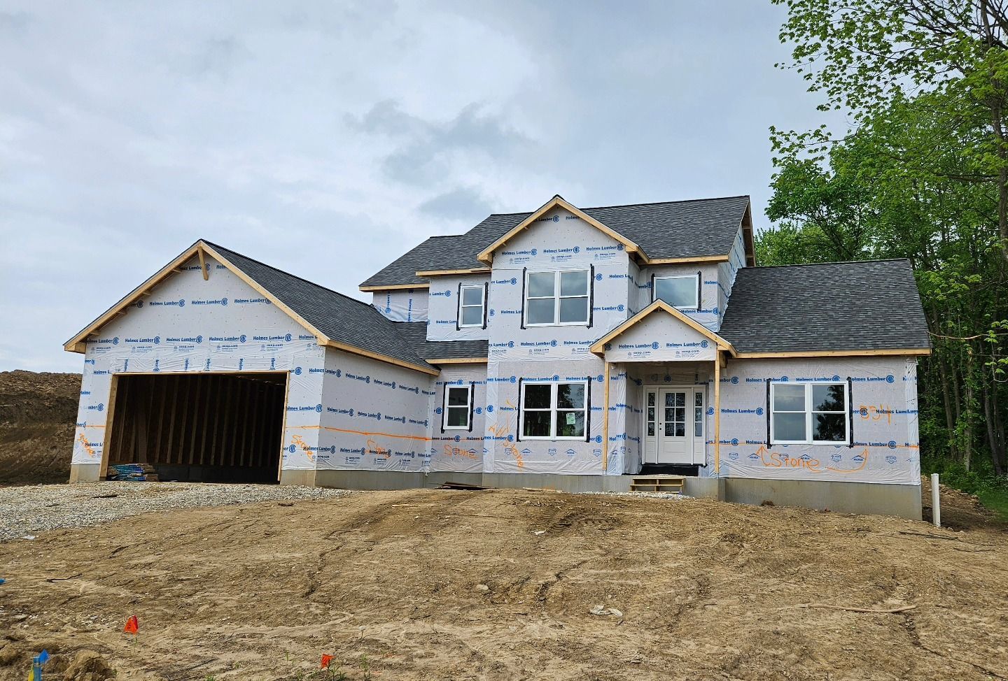 Two-story house under construction, covered in blue and white wrap, with a grey roof and garage.