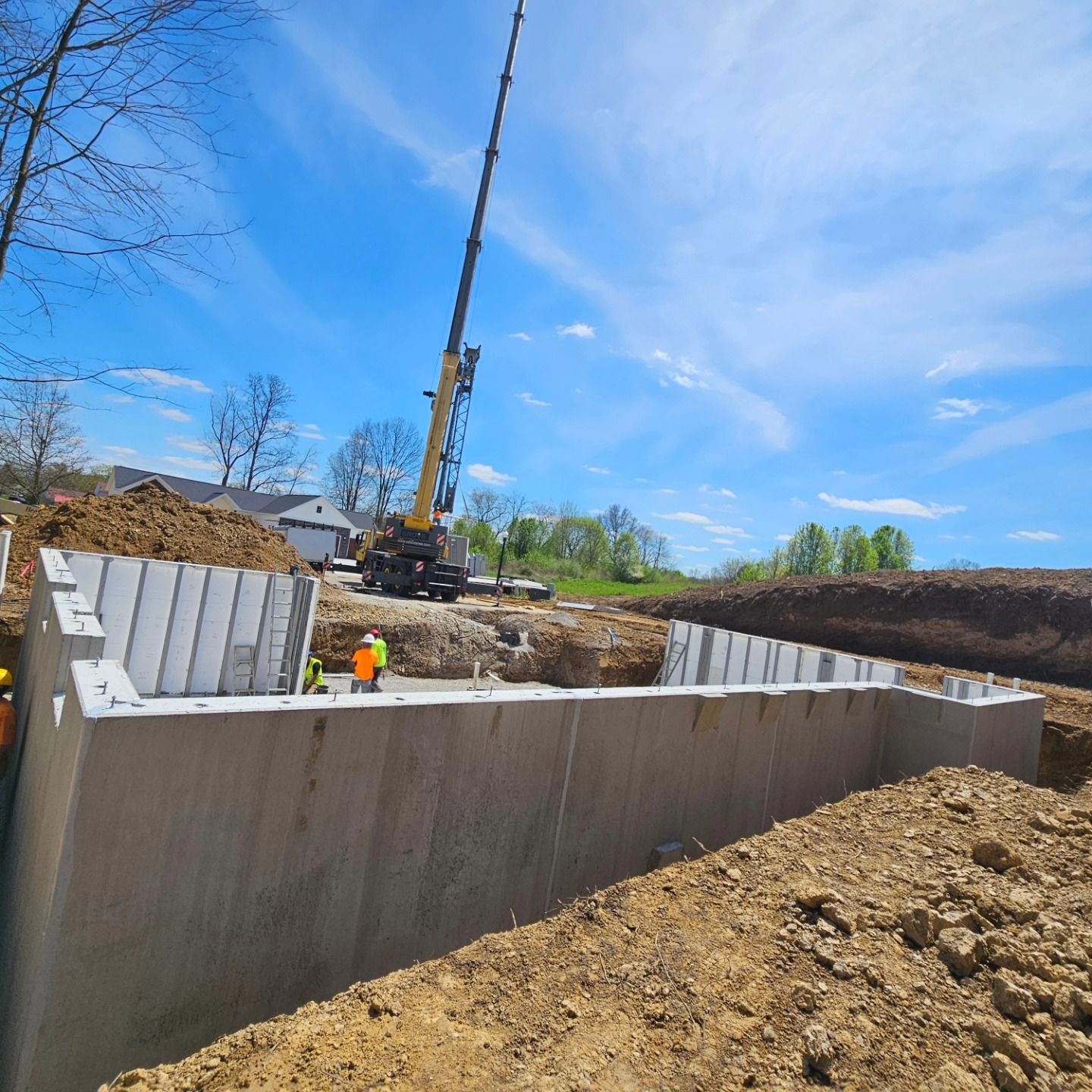Construction site with concrete foundation walls being built; crane and workers present.