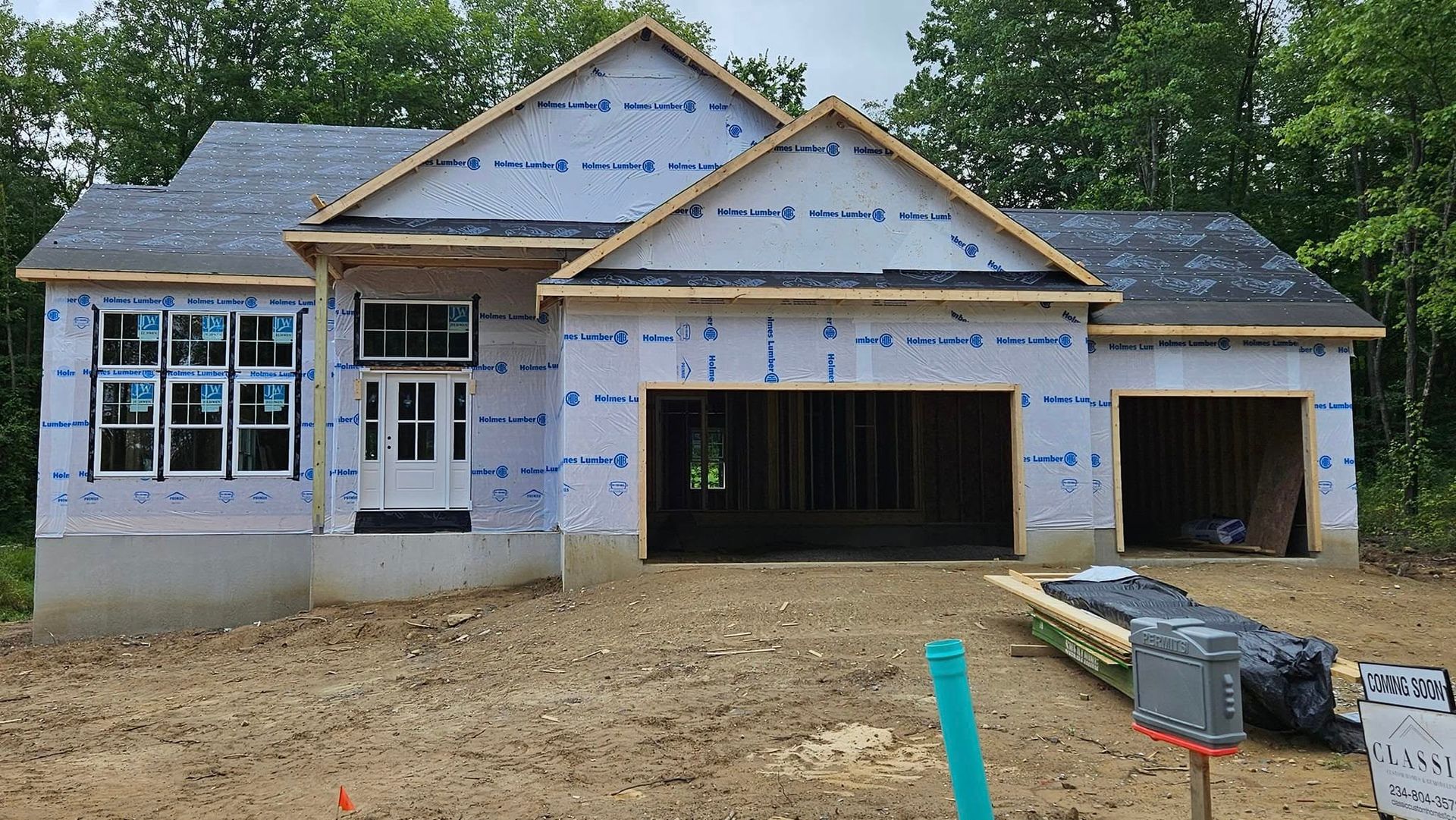 House under construction with garage doors, multiple windows, and a dark roof.