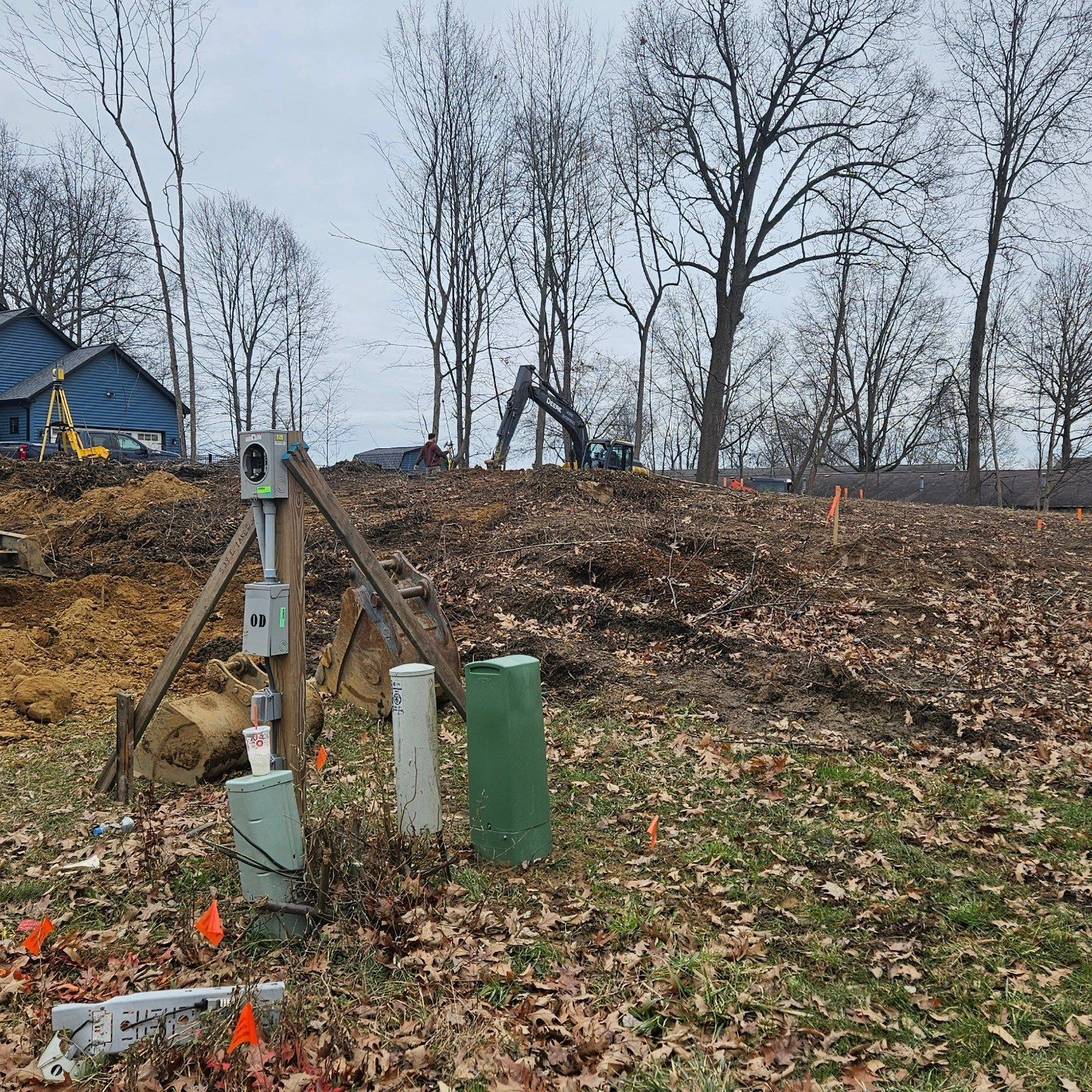 Construction site with electrical boxes, wooden supports, and heavy machinery, preparing land for development.