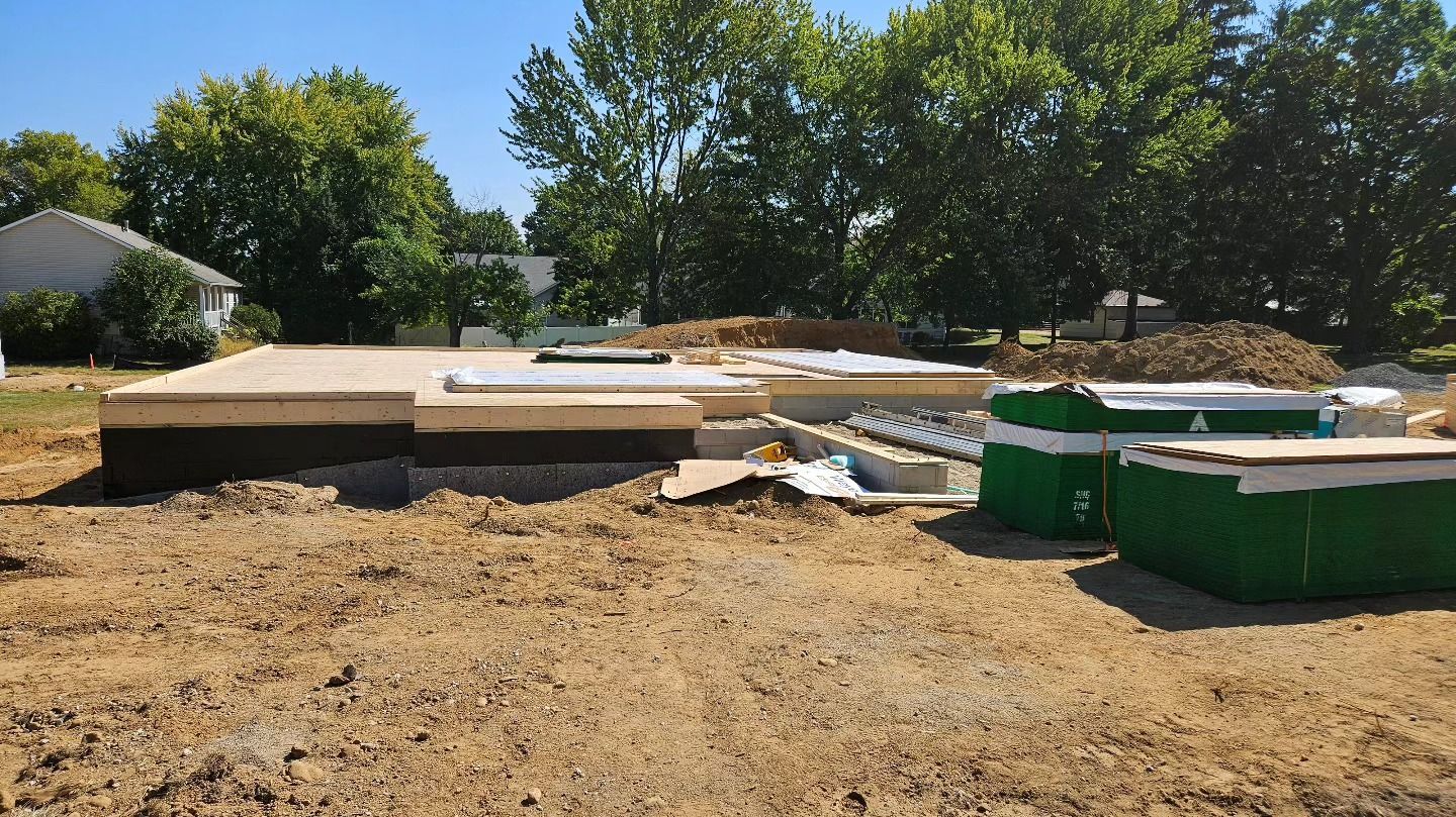 Construction site with a concrete foundation, dirt ground, and green building materials.