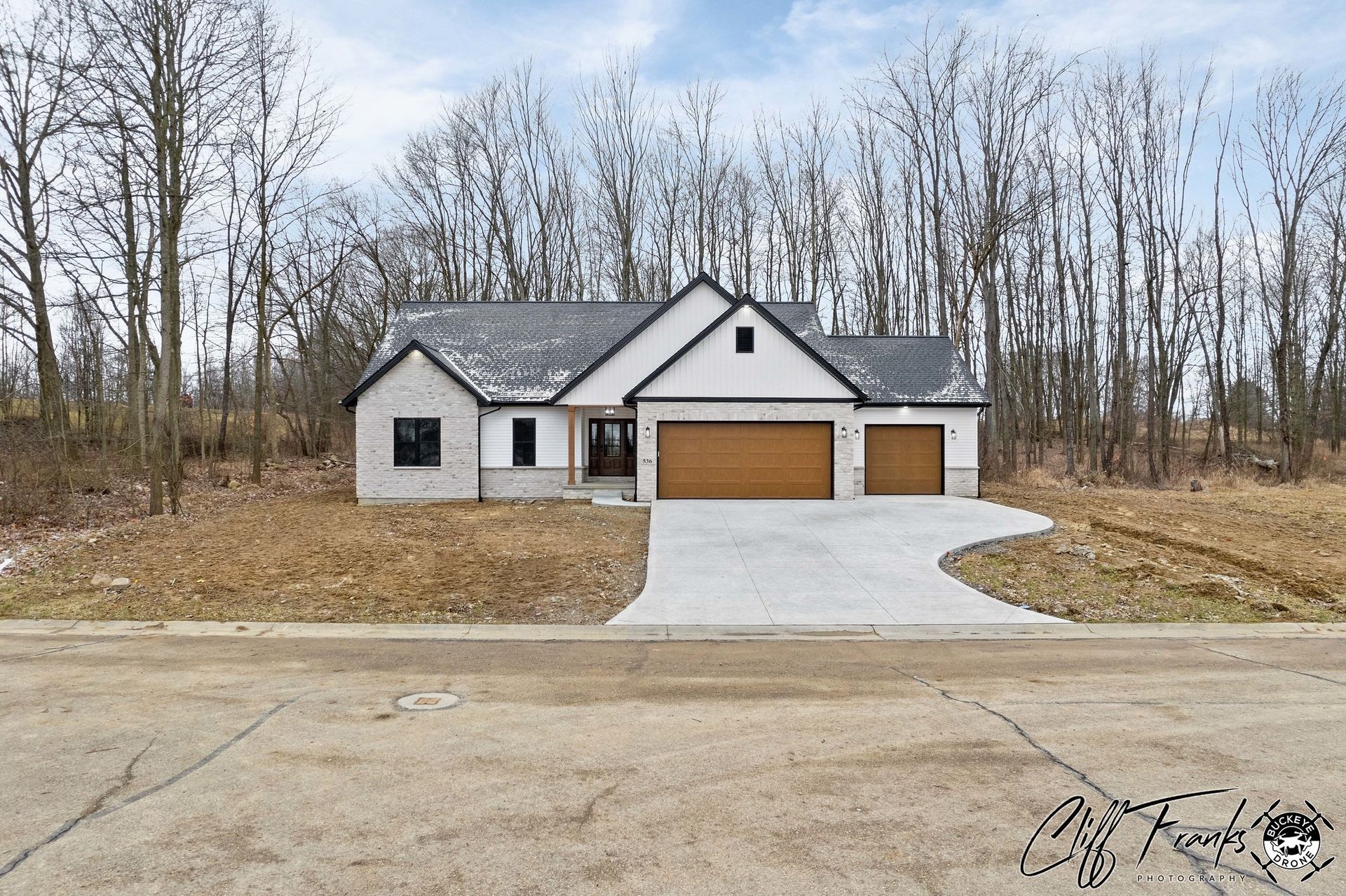 Modern house with gray brick, white siding, and tan garage doors; long concrete driveway.