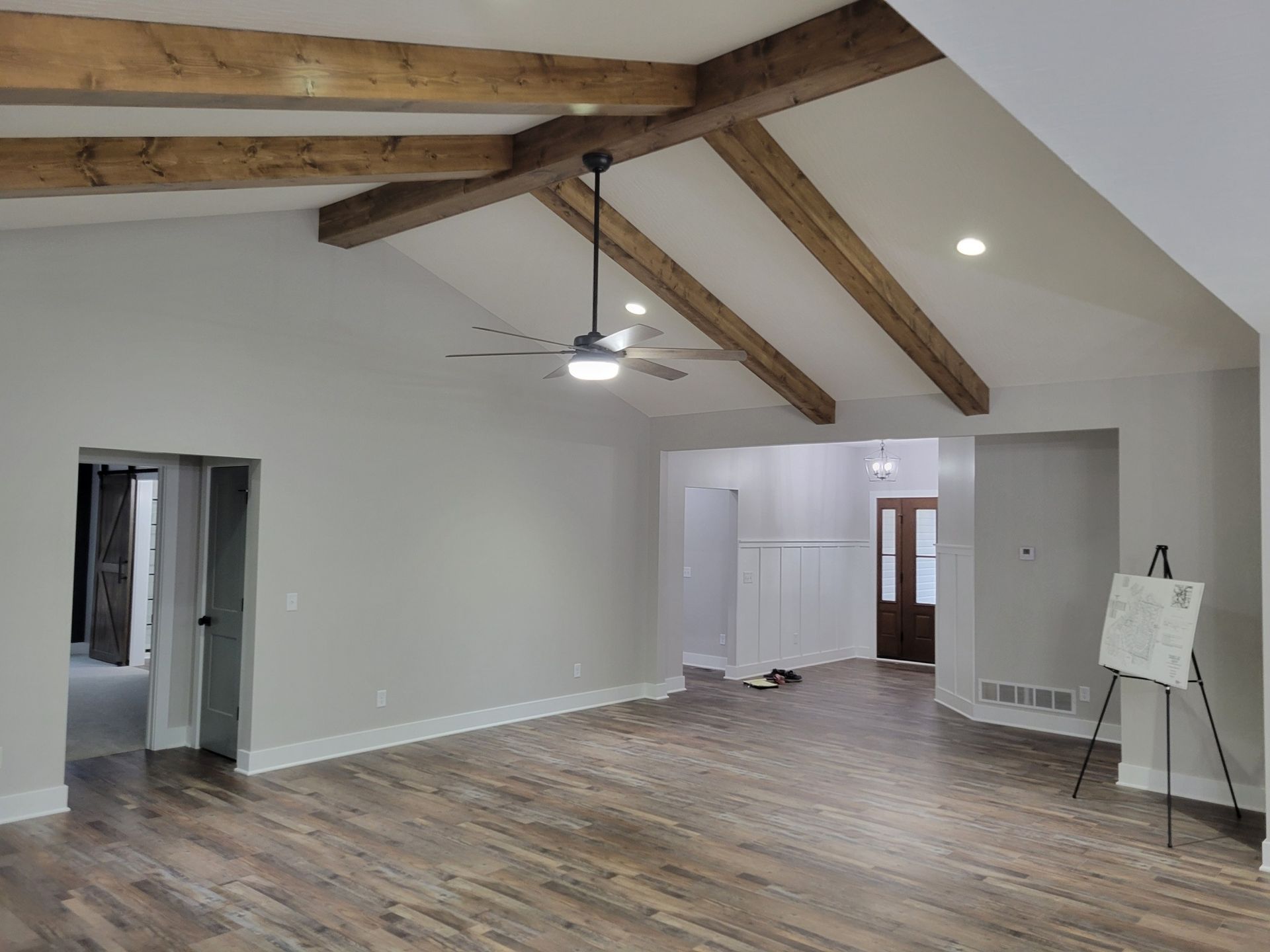 Spacious living room with wood beams on a sloped ceiling, wood-look flooring, and a ceiling fan.