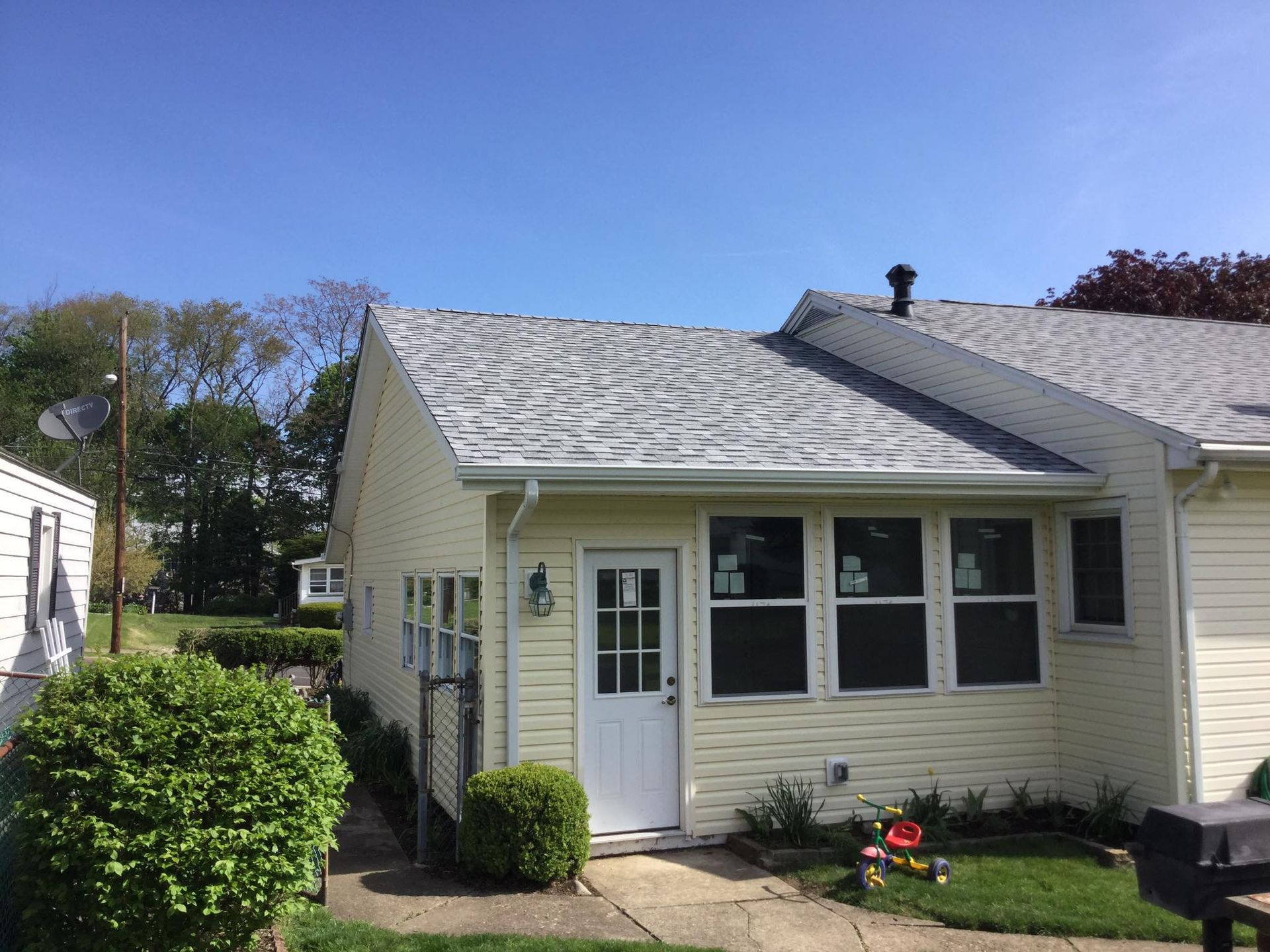 Yellow house with a gray shingled roof, a white door, and several windows under a blue sky.
