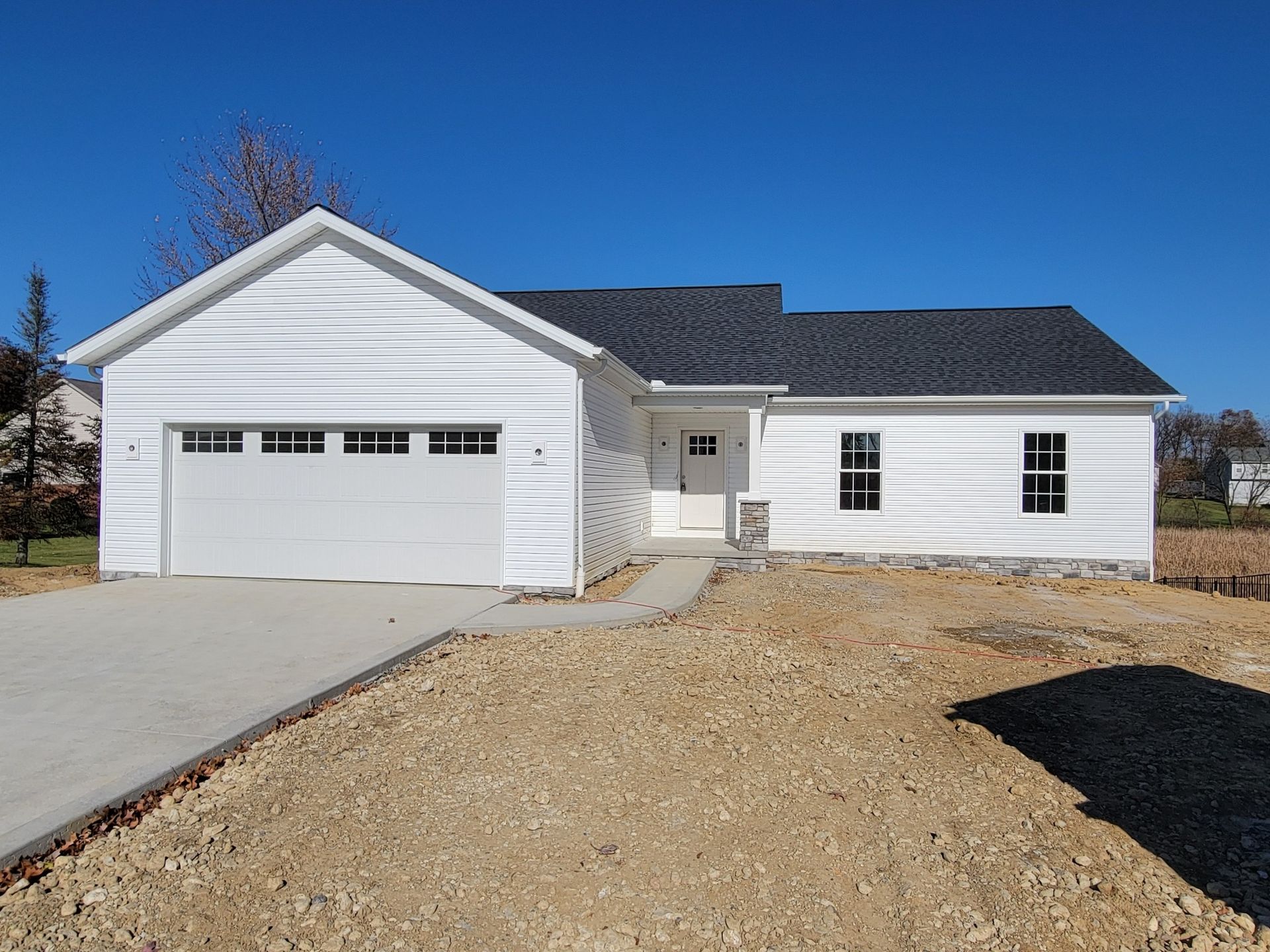 White house with attached garage, concrete driveway, and bare yard under a bright blue sky.