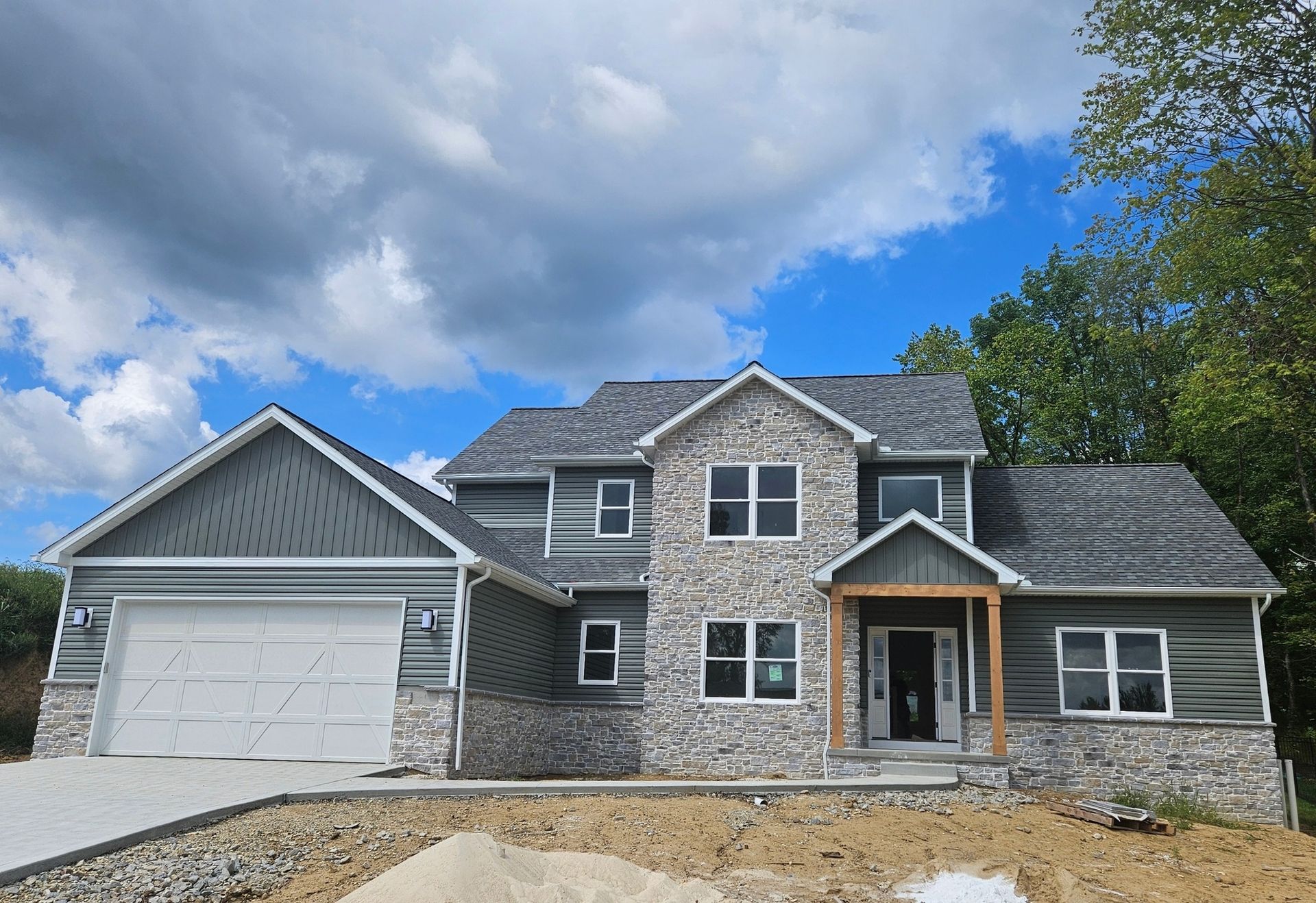 Two-story house with gray roof and siding, stone facade, and attached garage under a cloudy sky.