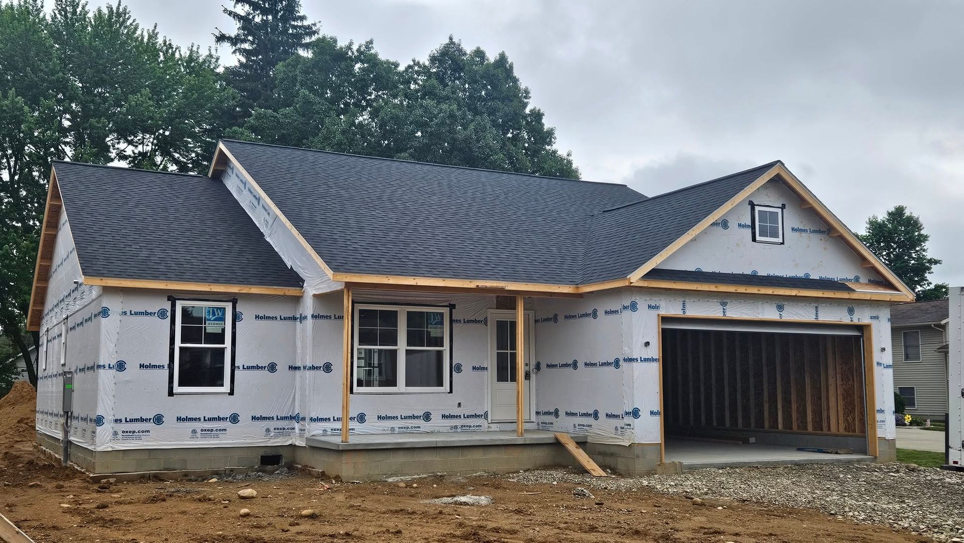 New house under construction; gray roof, blue wrap, unfinished garage and windows.