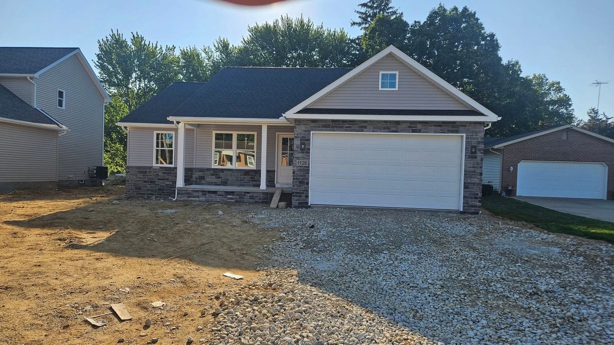 New house with stone and tan siding, a one-car garage, and gravel yard under construction.