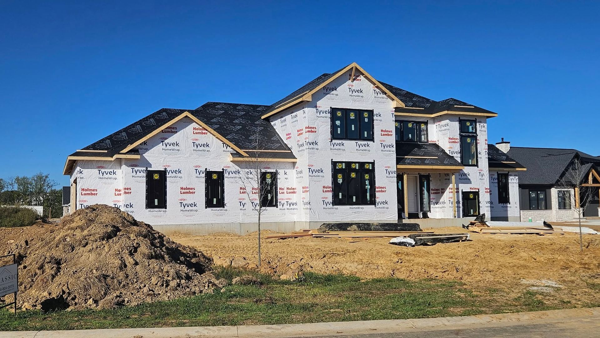 House under construction with black windows and dark roof, on a sunny day.