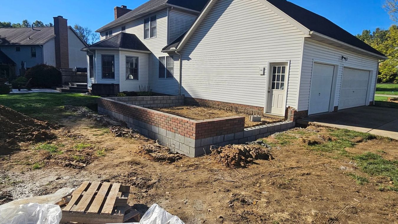 Brick and cinder block raised garden bed under construction near a house with a garage.