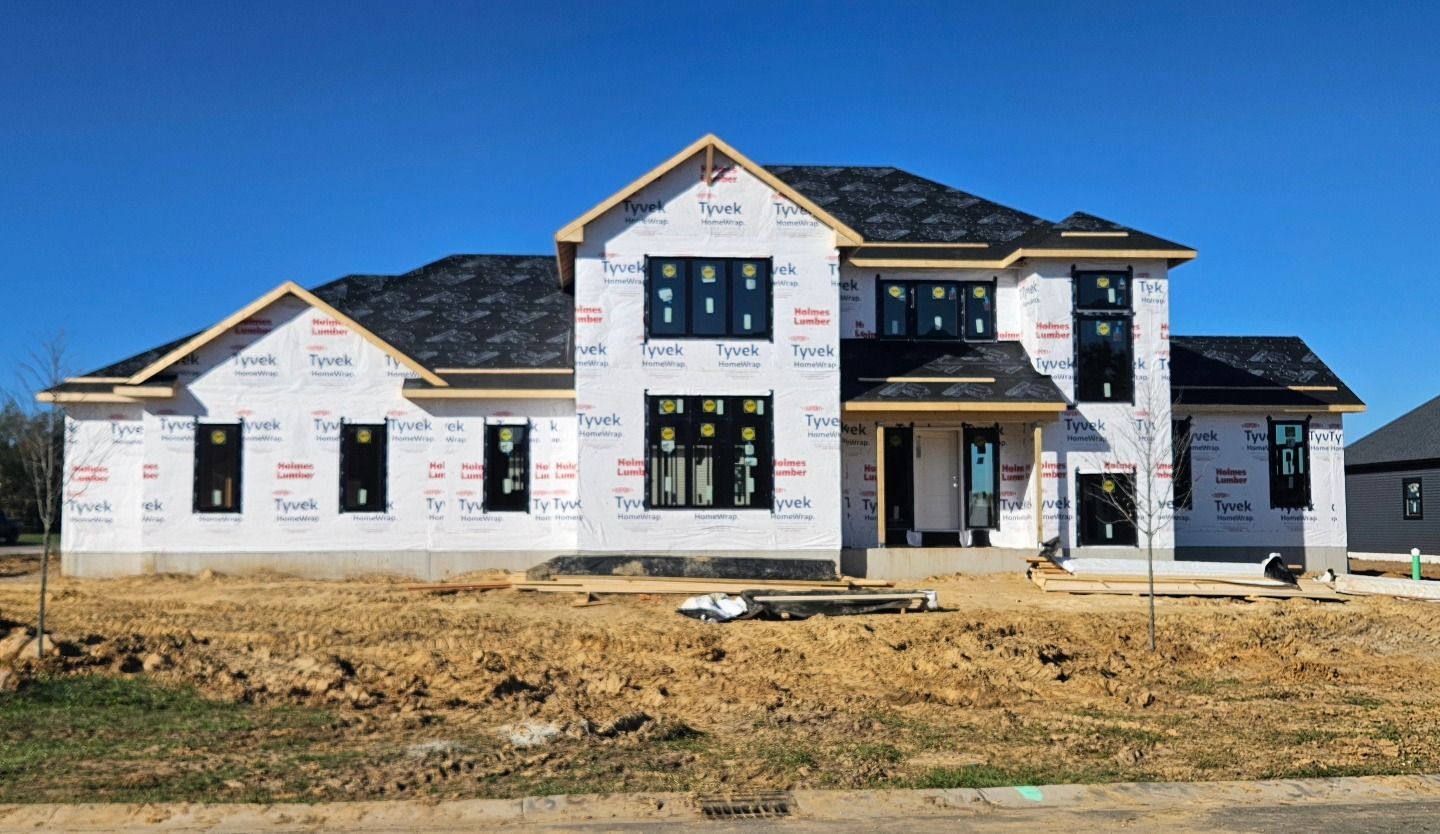 New house under construction with black windows and roof, wrapped in white protective covering, set in a dirt lot.