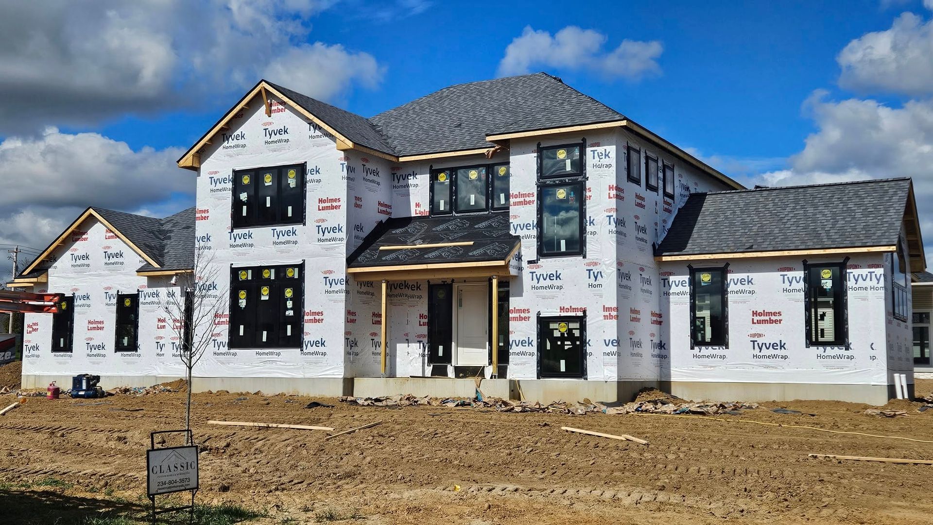 House under construction, covered in protective wrap, with black windows and gray roof.