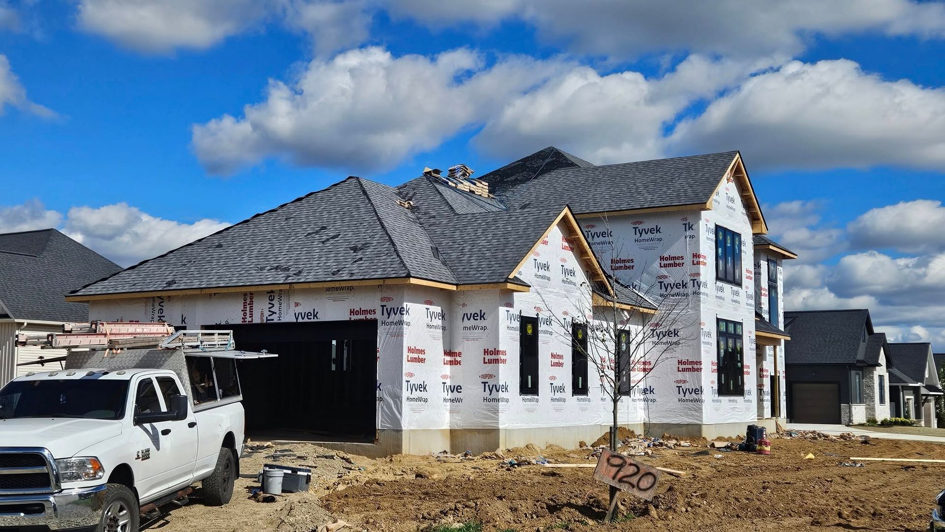 House under construction with installed roof, tarp-covered walls, and a white truck parked in front.