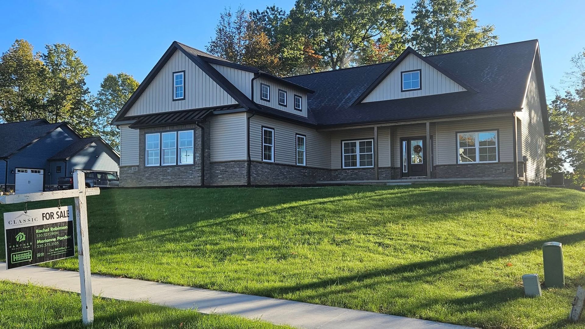 New house with green lawn, stone and tan siding, black roof, and 