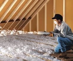 A man is kneeling down in an attic filled with insulation.