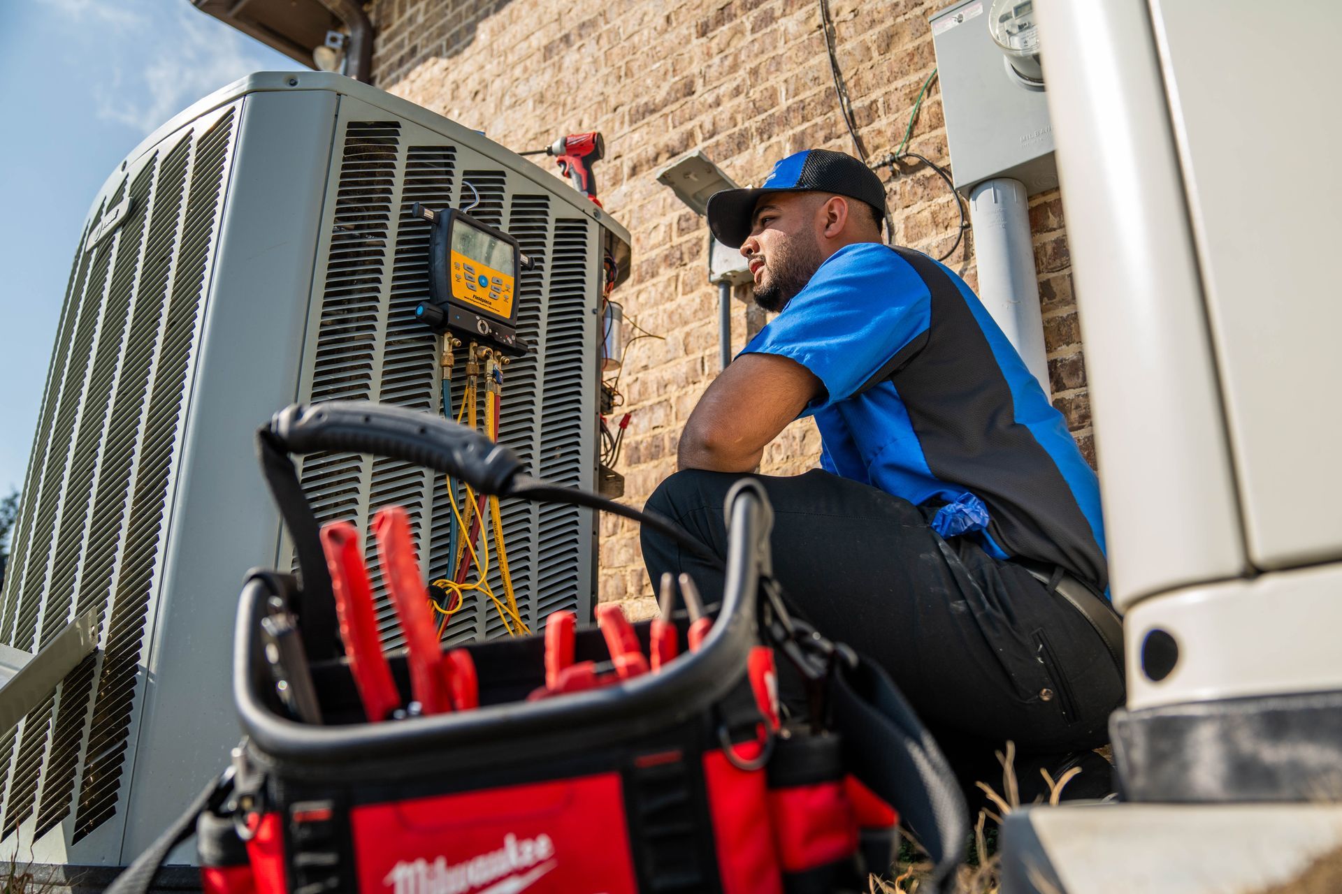 Two men are standing next to each other in front of an air conditioner.