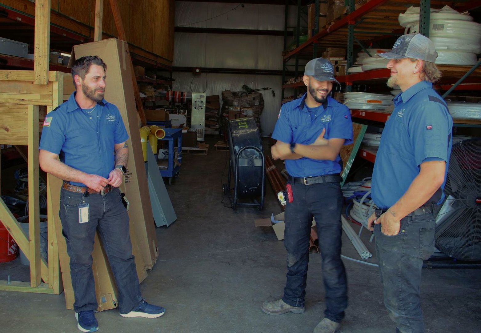 Three men are standing in a warehouse talking to each other.