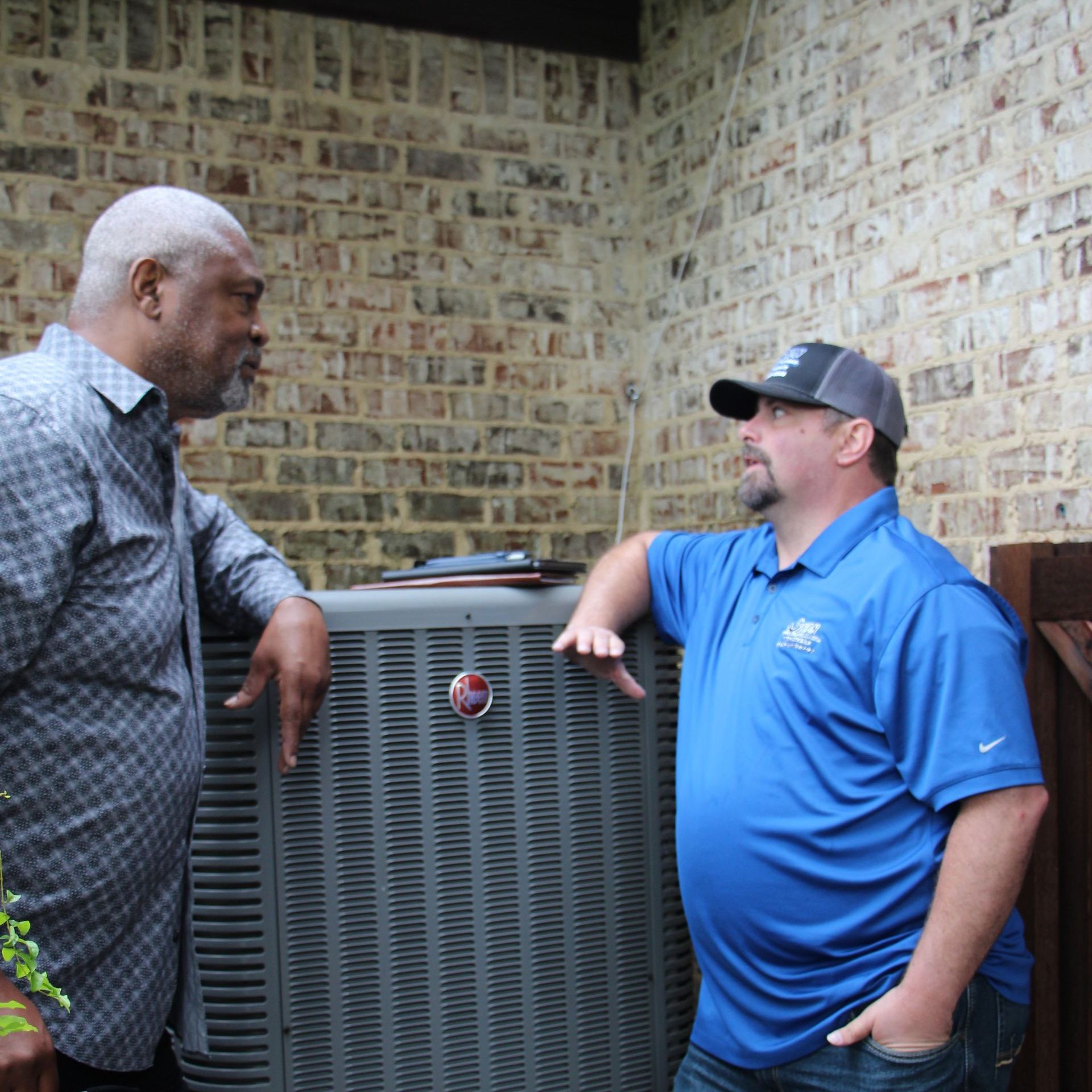 Two men are standing next to each other in front of an air conditioner