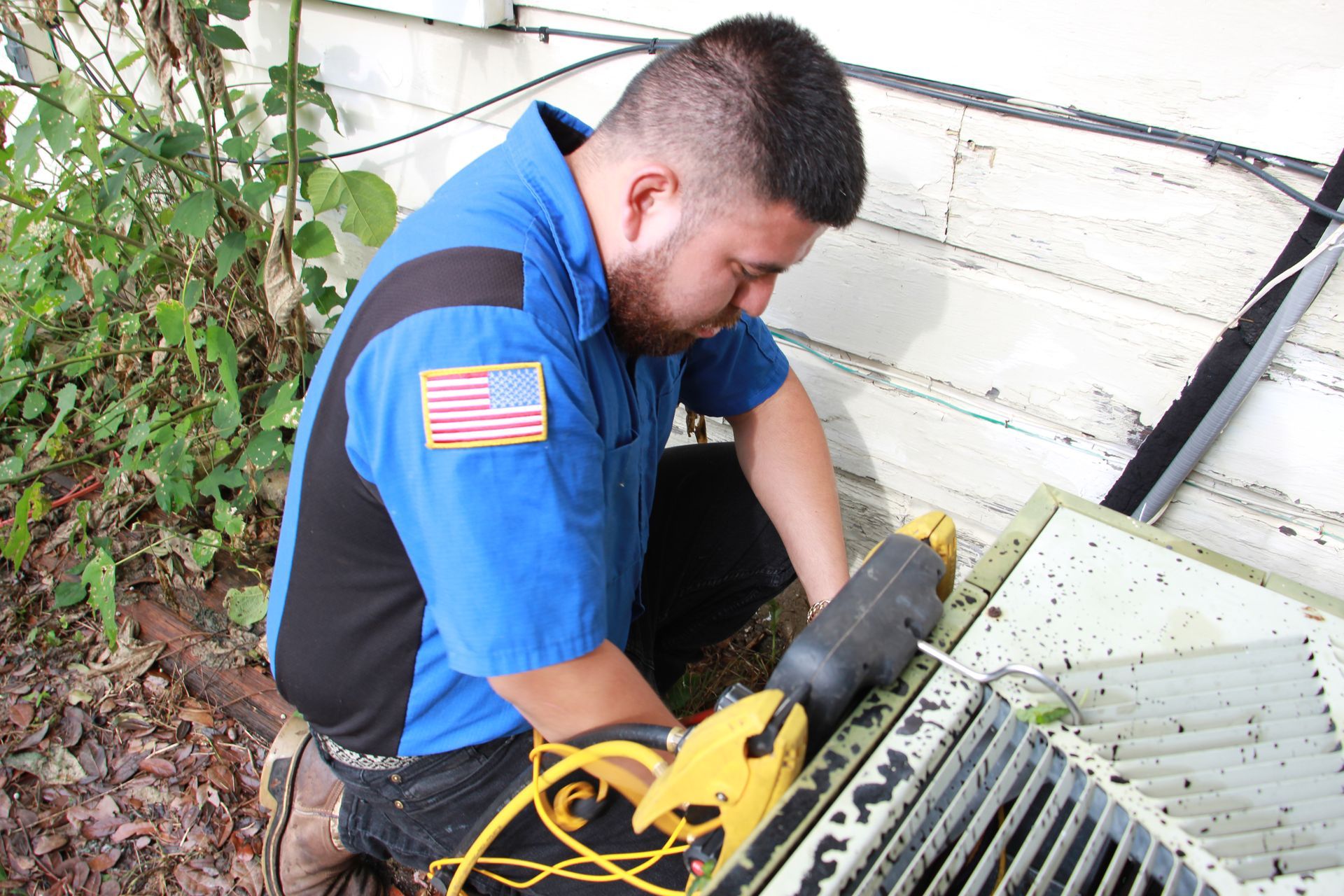 A man in a blue shirt is working on an air conditioner.