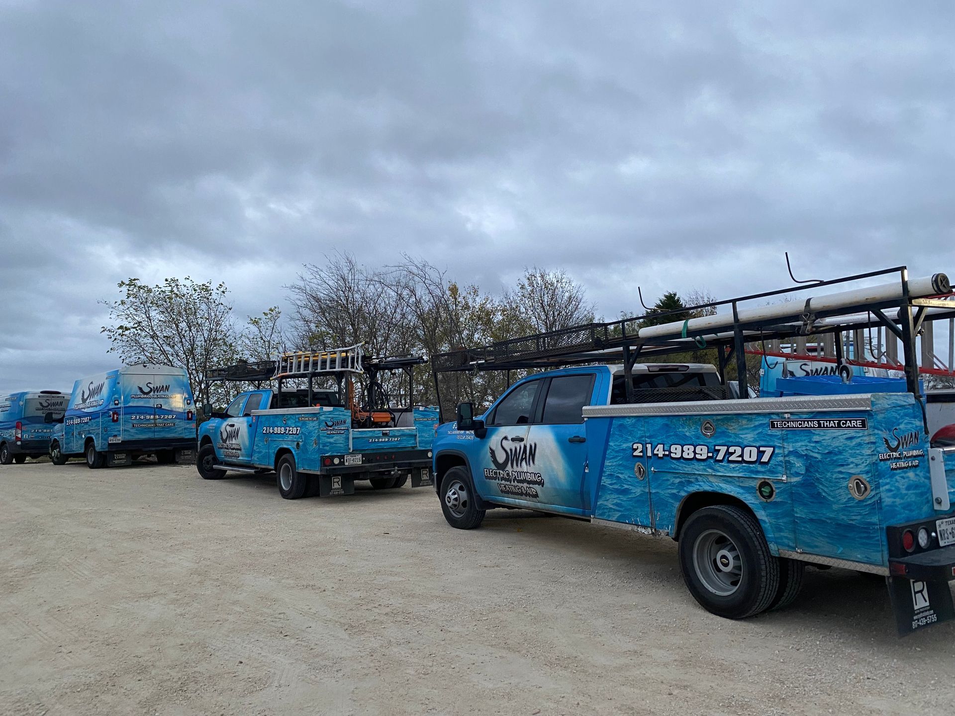 A row of blue trucks are parked in a gravel lot.