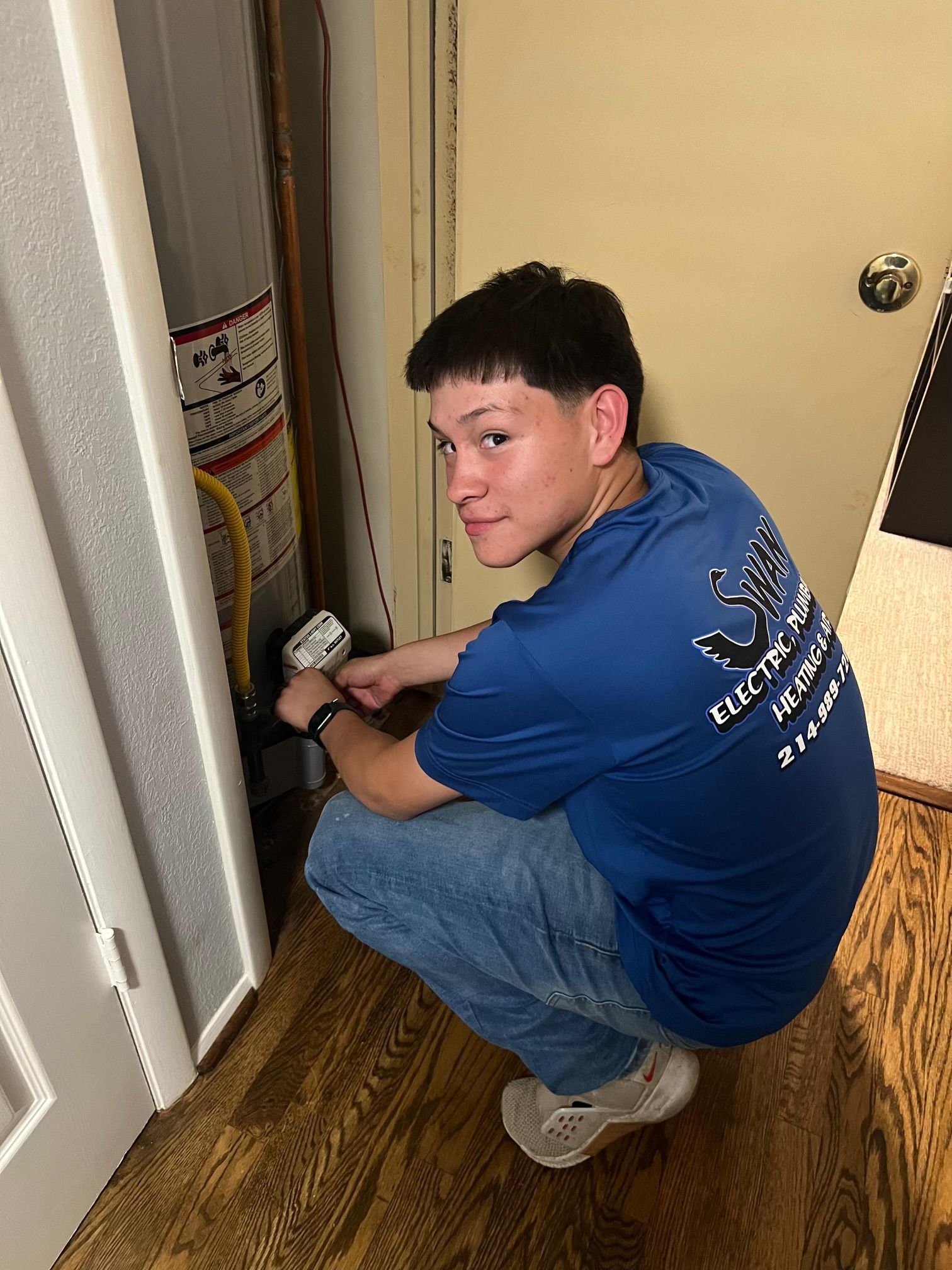 A man in a blue shirt is kneeling down in front of a water heater.