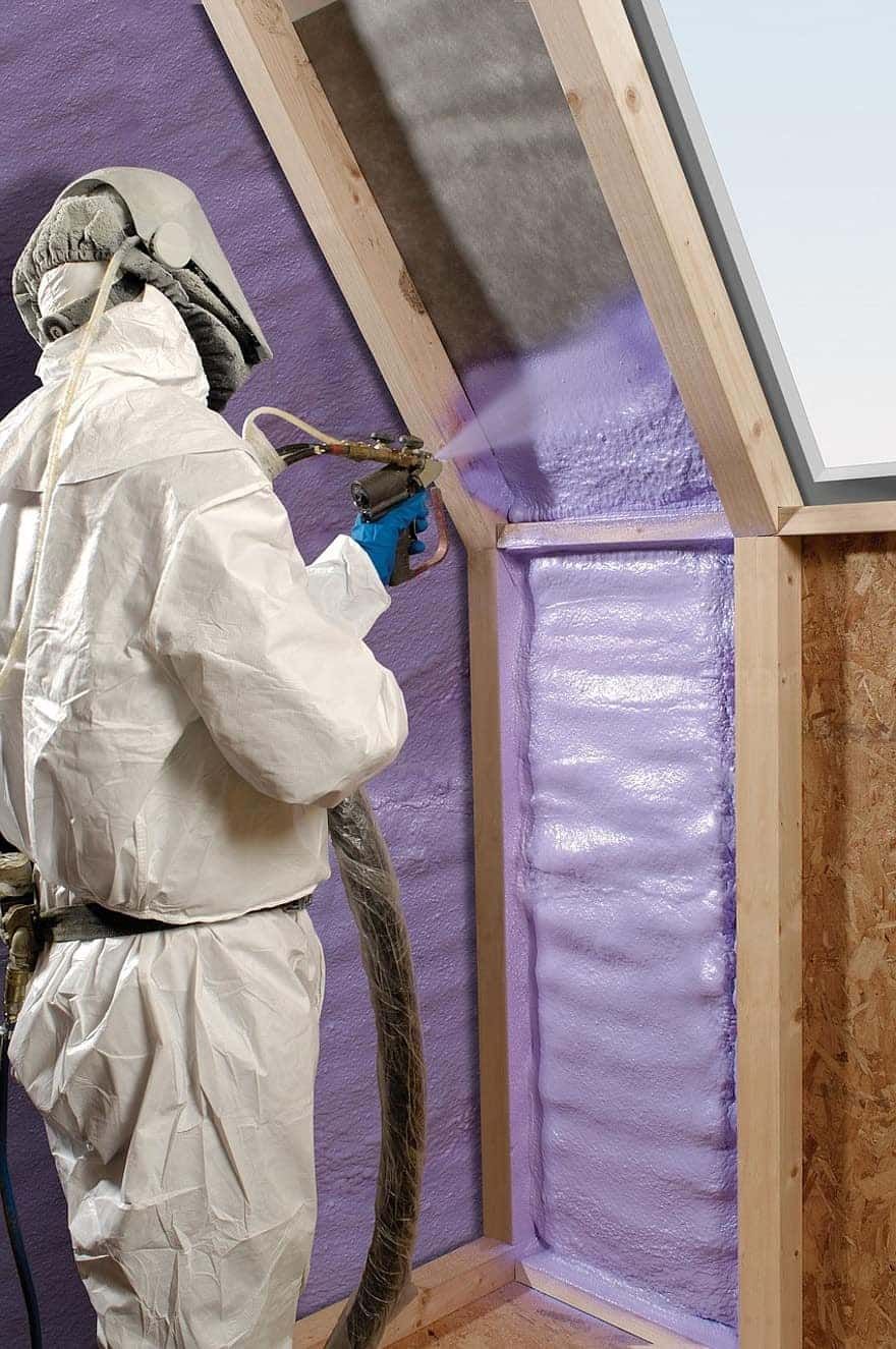 A man in a protective suit is spraying foam on a wall.