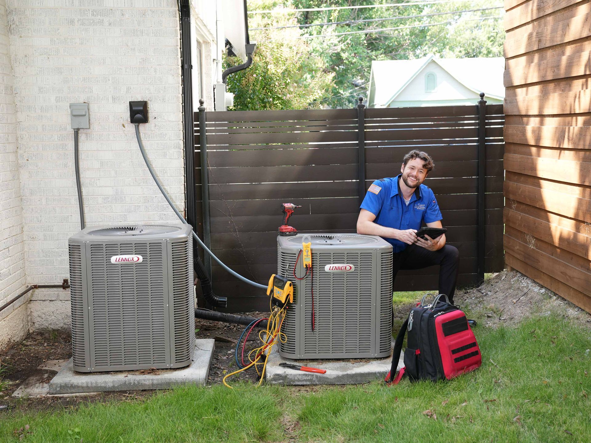 Two men are standing next to each other in front of an air conditioner.