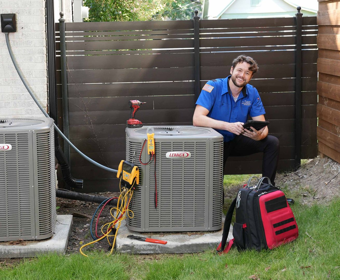Two men are standing next to each other in front of an air conditioner.