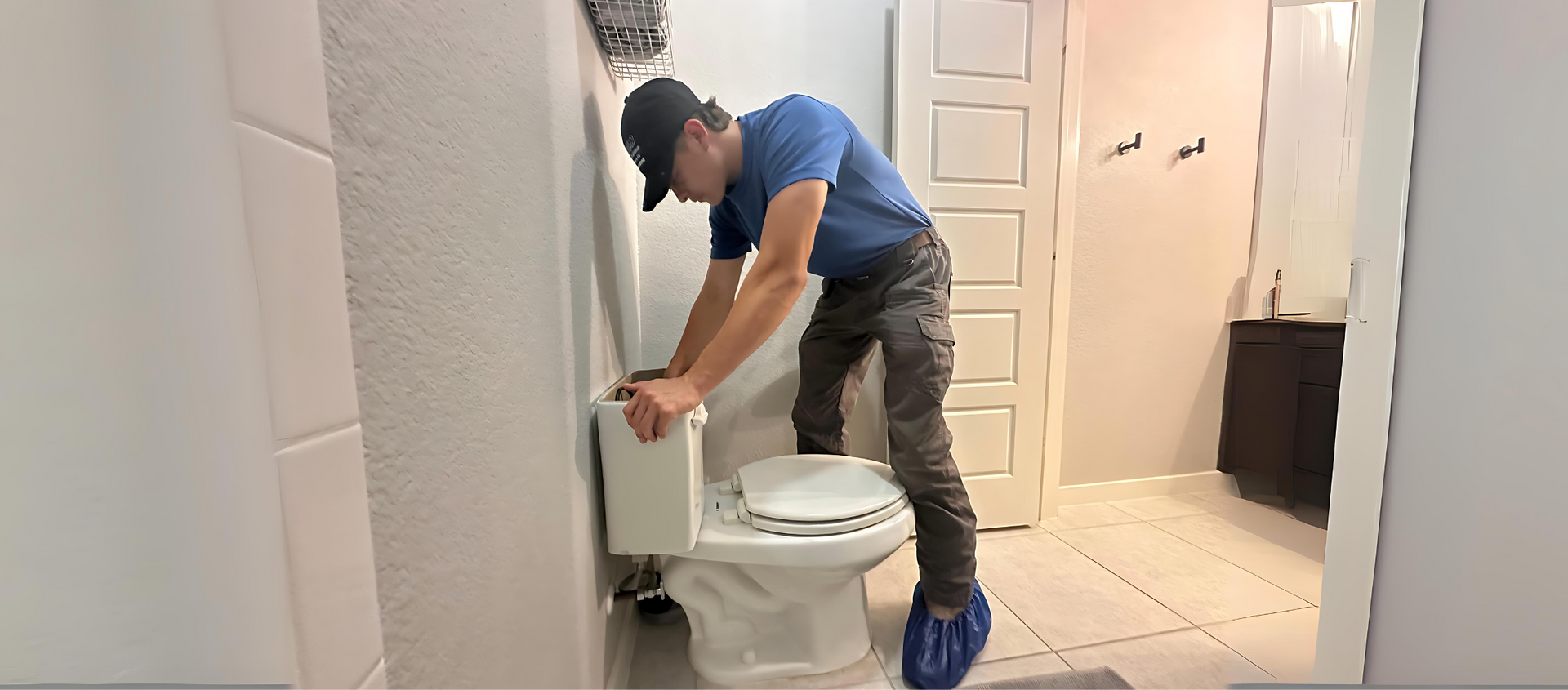 A man is standing next to a toilet in a bathroom.