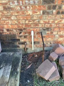 A pipe is connected to a brick wall next to a wooden picnic table.