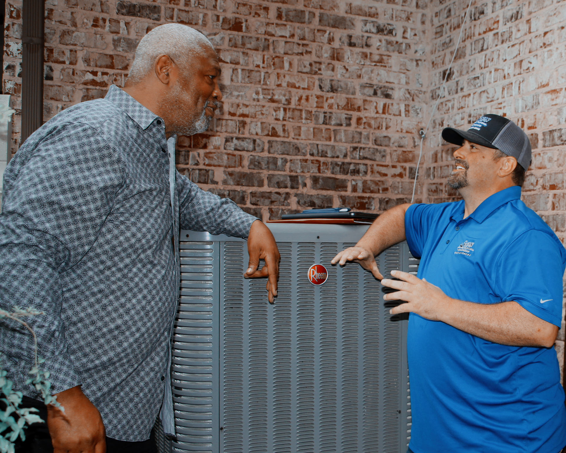 Two men are standing next to each other in front of an air conditioner.