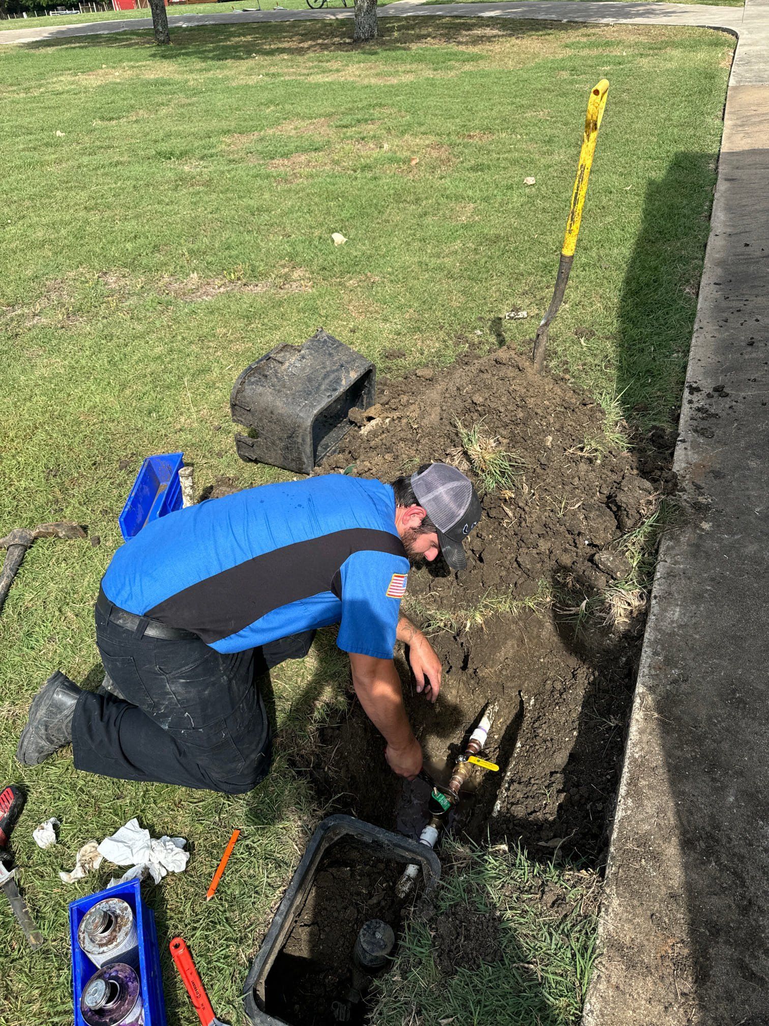 A man is kneeling down in the grass while working on a pipe.