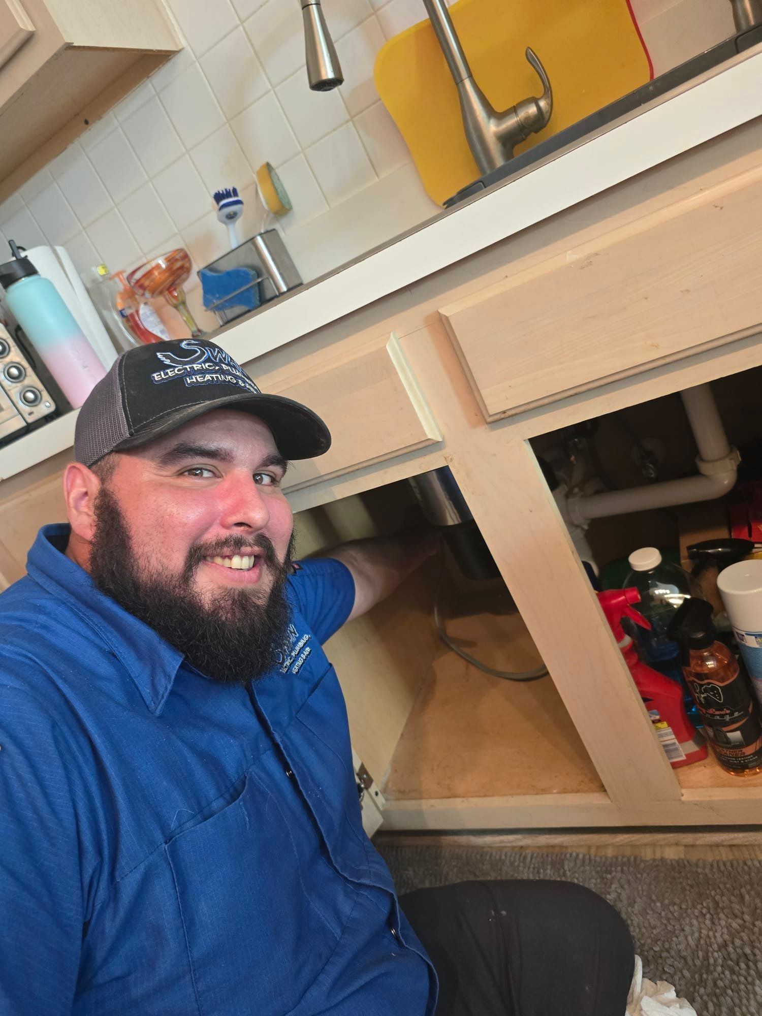 A man with a beard is kneeling under a sink in a kitchen.