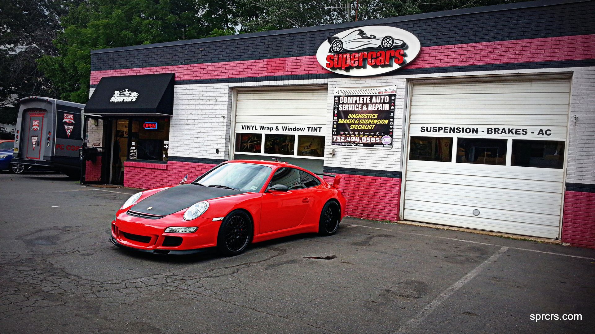 Red Porsche sports car parked in front of a garage, with a black roof.