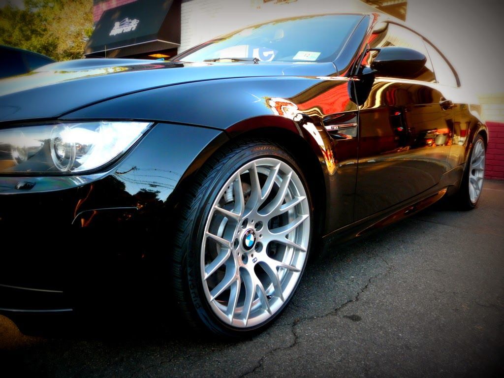Black BMW coupe with silver rims parked outdoors, reflecting surrounding buildings.