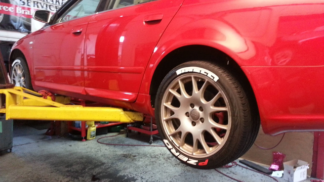 Red car on a yellow lift in a garage. Tire with white lettering.
