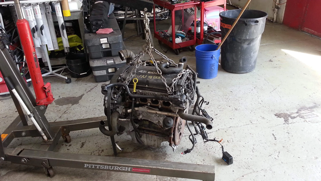 Engine suspended from a crane in a garage, ready for repair.