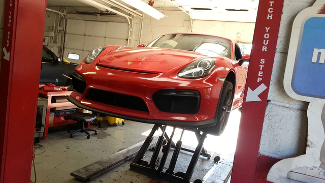 Red Porsche on a lift in a garage; arrow sign advises 