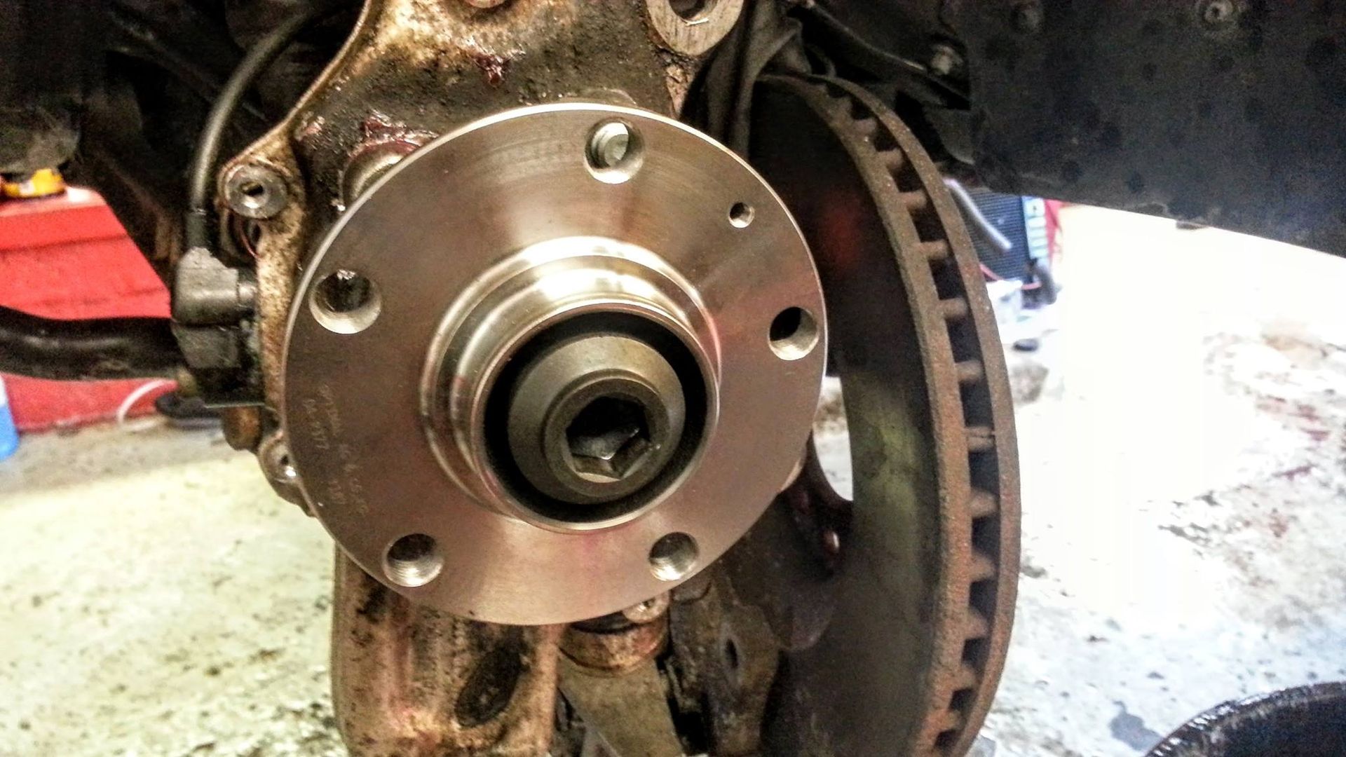 Car wheel hub assembly; silver hub with five bolt holes, rusty components in a repair setting.