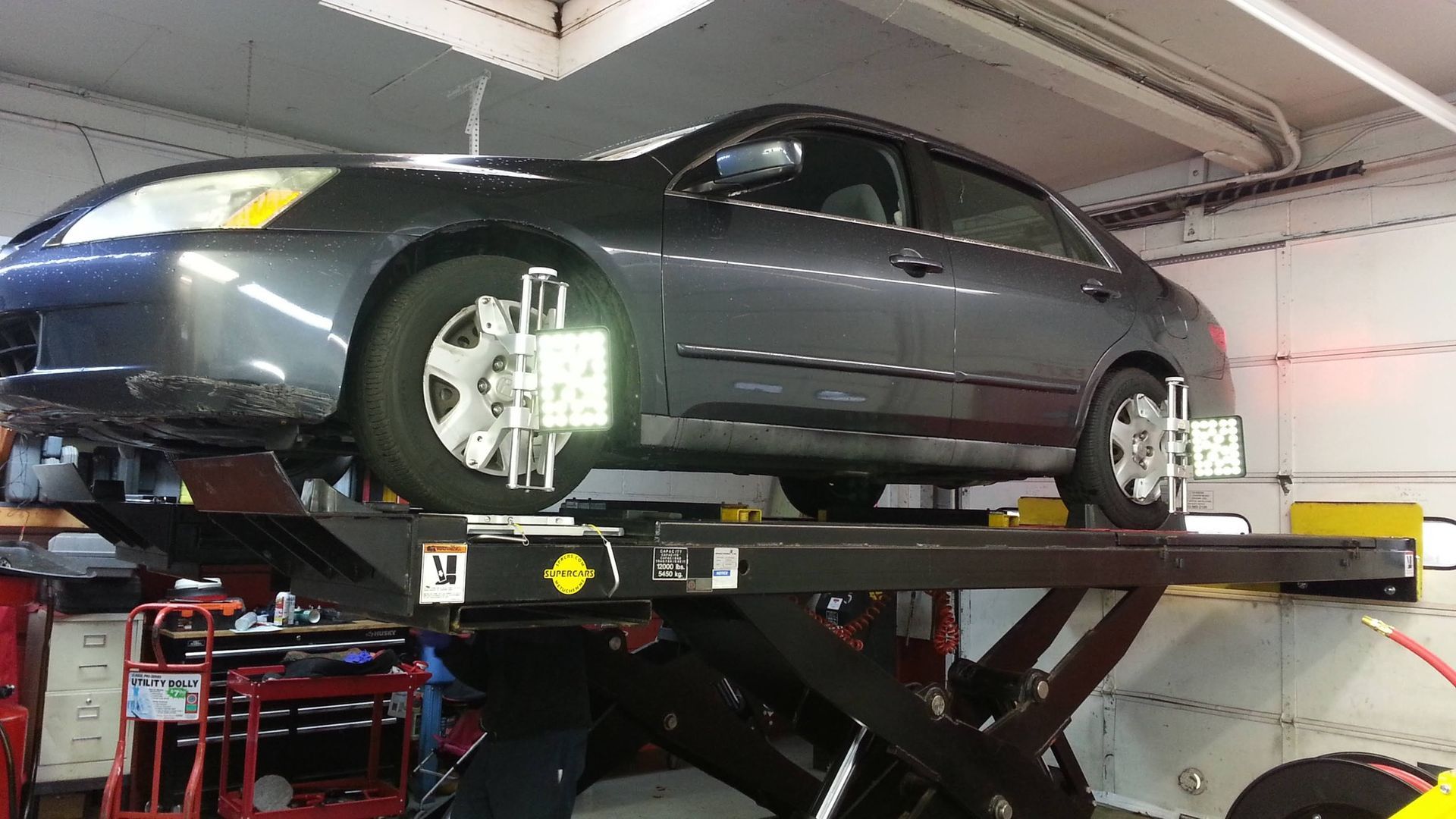 Gray car on a lift, undergoing wheel alignment in a garage.
