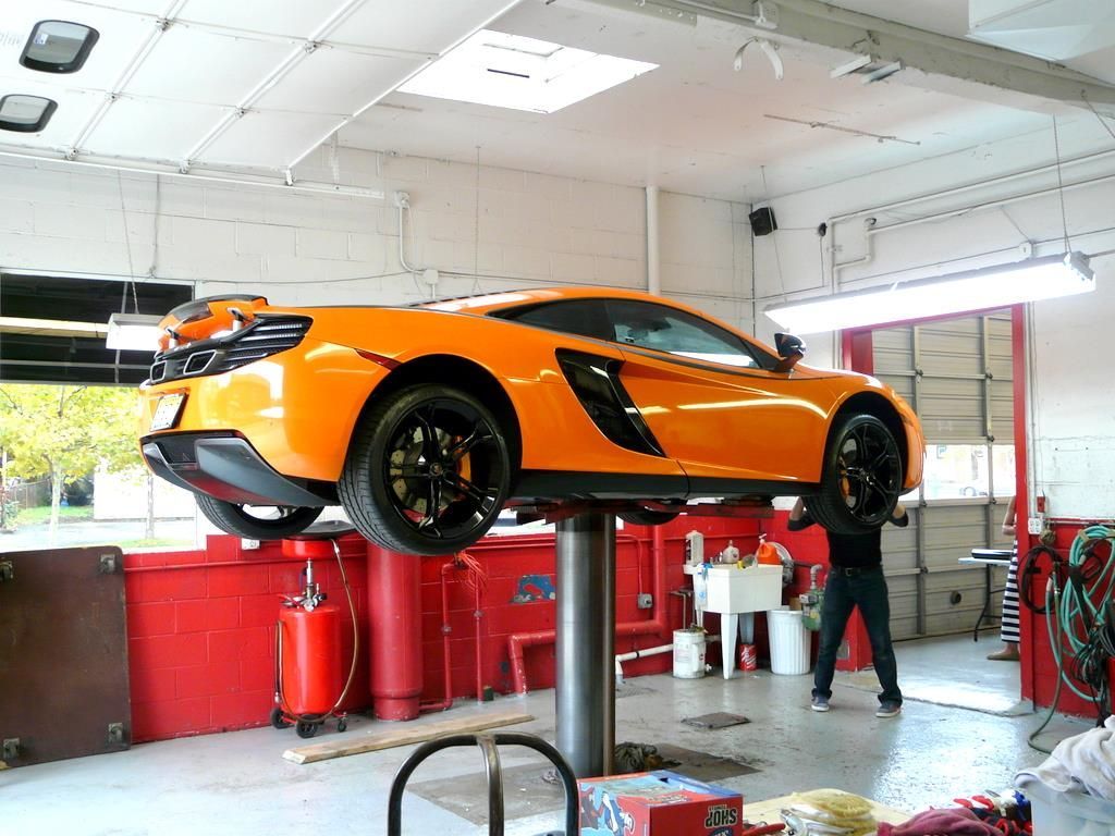 Orange McLaren sports car on a lift in a garage, being worked on by a mechanic.