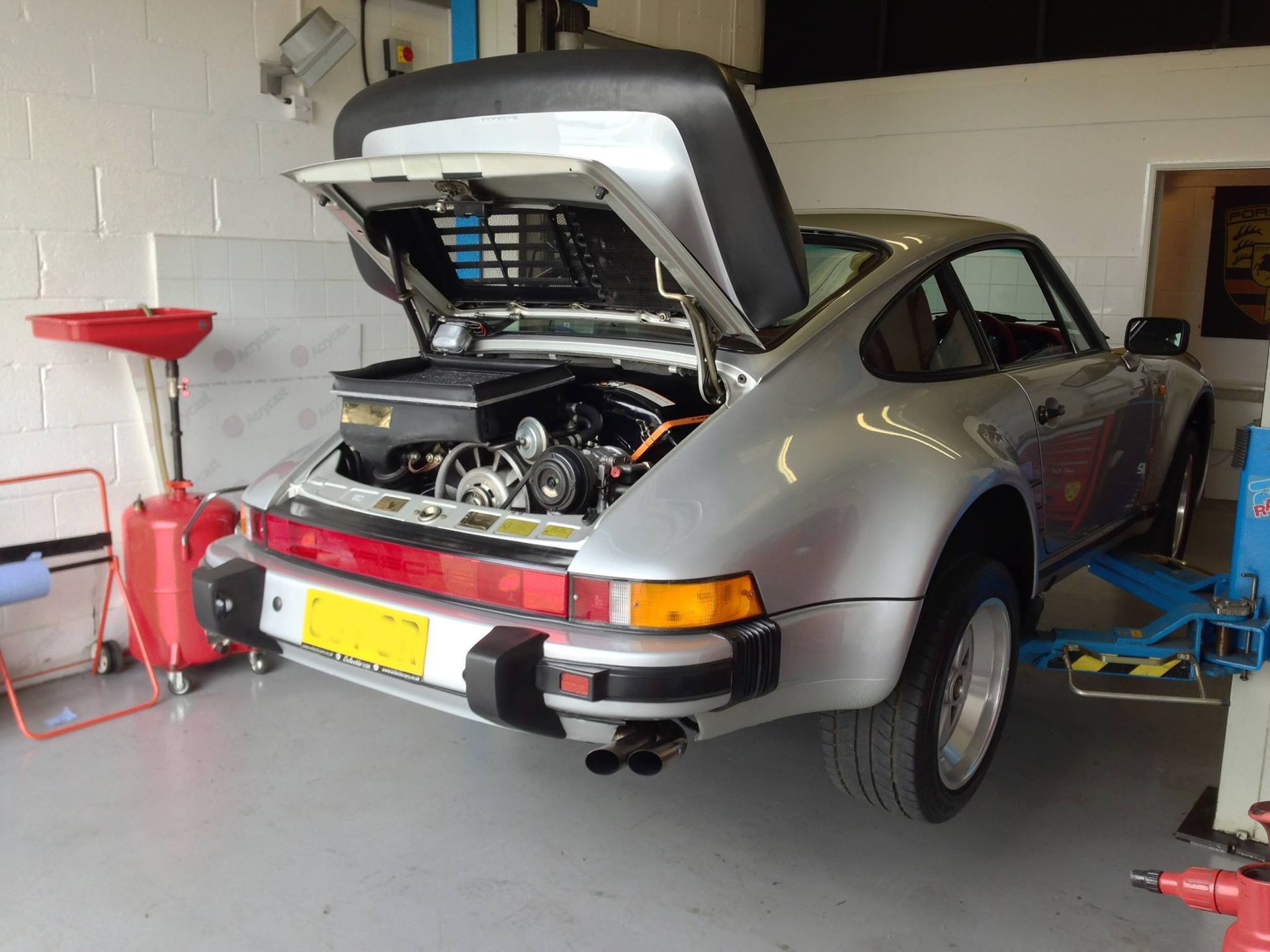 Silver Porsche 911 with open engine bay, in a garage, ready for service.
