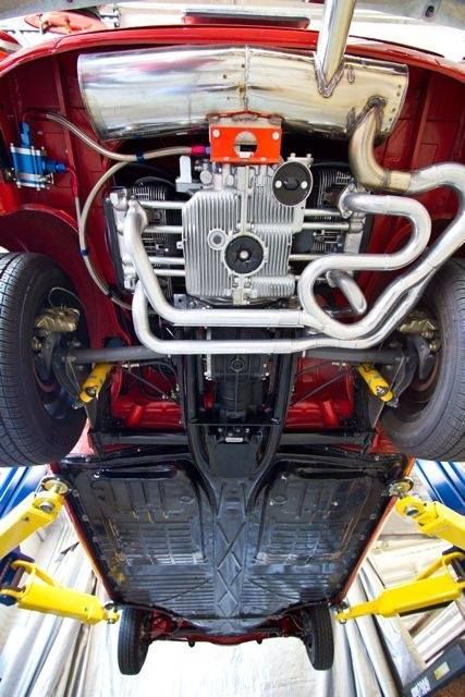 Red classic car raised on a lift, showing underside with engine, exhaust, and chassis details.