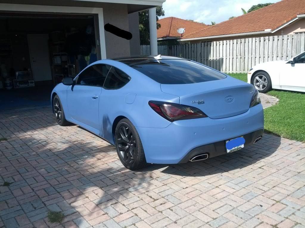 Blue coupe car parked in a driveway with a garage in the background. Another car is parked on the right.