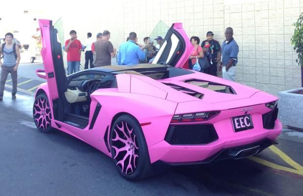 Pink Lamborghini convertible with open doors and custom wheels, parked with people looking on.
