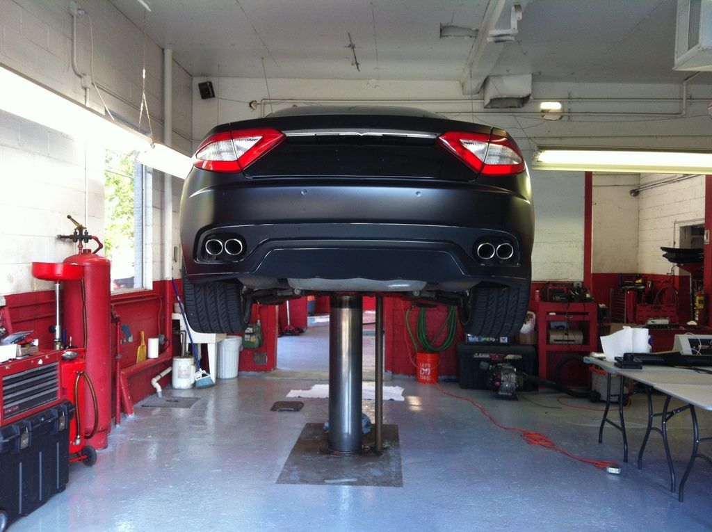 Black car raised on a lift in a mechanic's shop, revealing exhaust pipes.