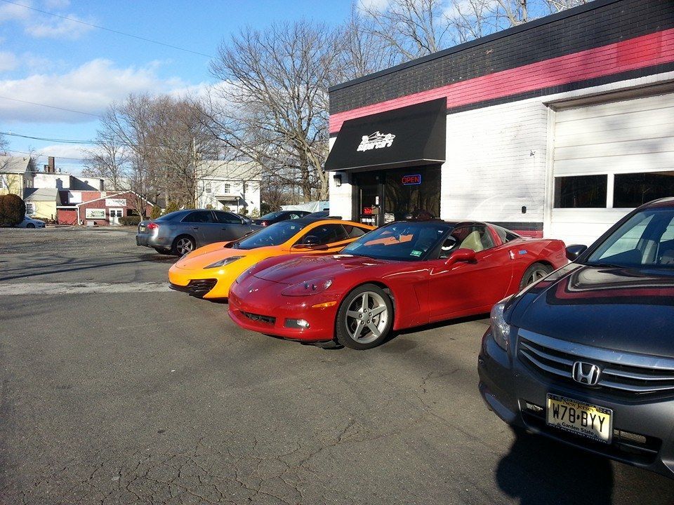 Row of sports cars in front of a business with a black awning, on a sunny day.
