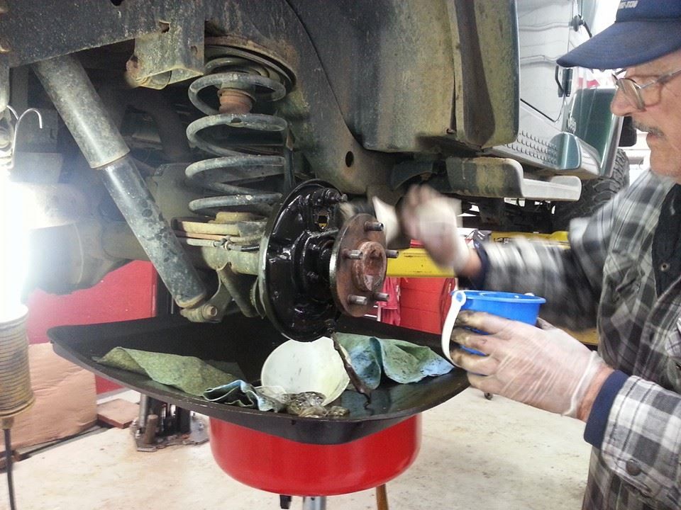 Man working on vehicle's brakes; uses oil pan to catch debris, workshop setting.