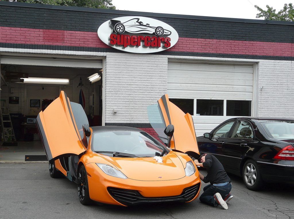 Orange McLaren with open doors parked outside a shop called 
